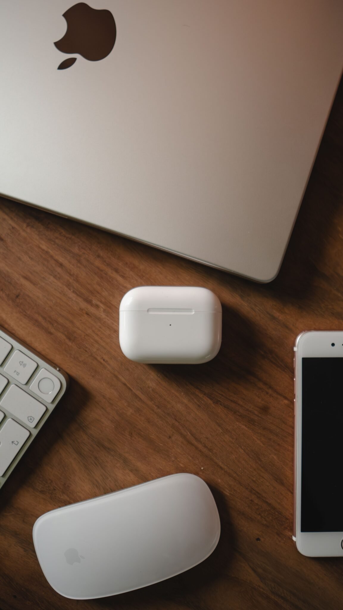A collection of Apple products including AirPods, MacBook, and iPhone on a wooden table.